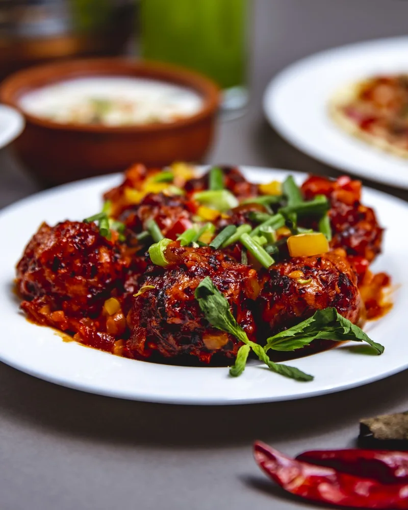 Chicken 65 in a glossy red sauce with spring onion, peppers and mint